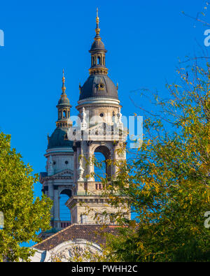 Les coupoles de l'- monument architectural de la basilique Saint-Étienne à Budapest. Vue sur l'Église à travers le feuillage des arbres. Banque D'Images