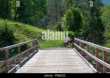 Cycliste traverse un pont de bois sur la rivière Inn à Scuol, dans le canton suisse des Grisons Banque D'Images