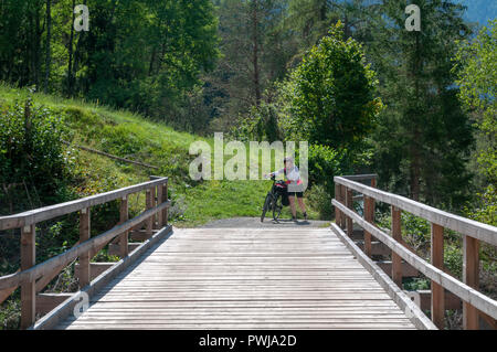 Cycliste traverse un pont de bois sur la rivière Inn à Scuol, dans le canton suisse des Grisons Banque D'Images