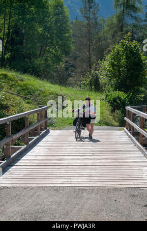 Cycliste traverse un pont de bois sur la rivière Inn à Scuol, dans le canton suisse des Grisons Banque D'Images