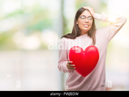 Young hispanic woman holding heart in love a souligné avec la main sur la tête, choqué par la honte et la surprise face, en colère et frustrés. La peur et la colère pour Banque D'Images