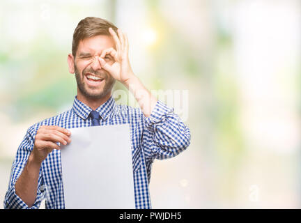 Beau Jeune homme tenant le papier blanc sur fond isolé avec happy smiling face ok faire signe avec la main sur de l'oeil Banque D'Images