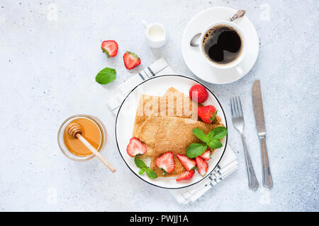 Crêpes ou blinis avec fraise, tasse de café et de miel. Délicieux petit déjeuner gastronomique, d'un bleu fond de béton. Vue d'en haut Banque D'Images