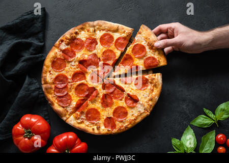 Cueillette à la main Tranche de pizza au pepperoni. Pizza Party. Nude italian pizza au pepperoni, sur fond de béton noir, vue du dessus Banque D'Images