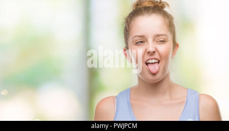 Young blonde woman sticking tongue out heureux avec drôle d'expression. Concept d'émotion. Banque D'Images