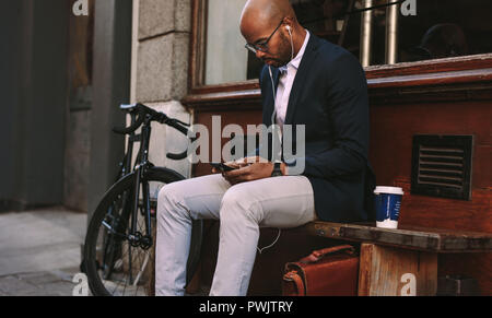 A l'extérieur de l'Afrique de l'chauve sur un banc à l'aide de téléphone. Man wearing earphones et écouter de la musique de téléphone smartphone. Banque D'Images