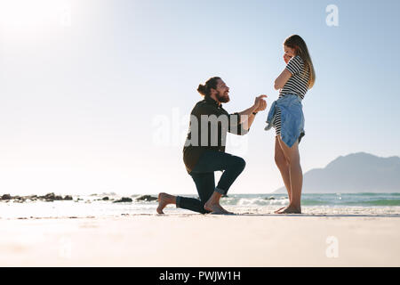 L'homme vers le bas sur un genou offrant une surprise à la femme. Homme Femme propose à la plage. Banque D'Images