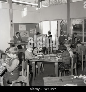 Années 1950, historiques, de jeunes garçons et filles ensemble à l'intérieur d'une salle de classe de faire un certain nombre d'activités éducatives et amusantes, telles que la peinture, d'énigmes et de l'artisanat à base de papier, England, UK. Banque D'Images