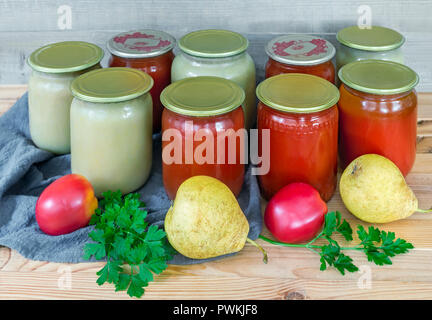 Purée de poire et le jus de tomate sont conservés dans des bocaux en verre avec couvercles métalliques scellés. Près de se coucher les poires et les tomates. Banque D'Images