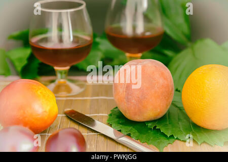 Still Life : sur la table sur les feuilles vertes sont les fruits, à côté de deux verres de vin. Banque D'Images