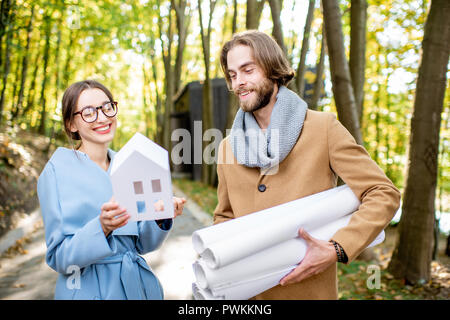 Couple créatif des architectes ou designers debout avec des dessins et modèle maison en plein air dans la forêt Banque D'Images