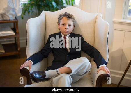 Boy wearing suit sitting in armchair Banque D'Images