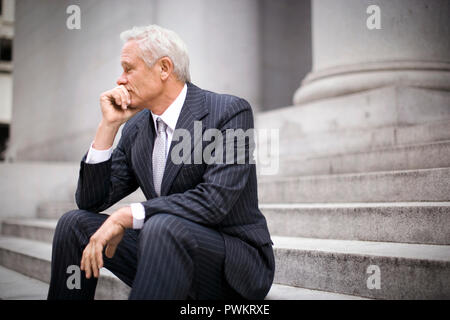 Mature businessman assis dehors sur les marches d'un bâtiment tout en appuyant son menton dans sa main. Banque D'Images