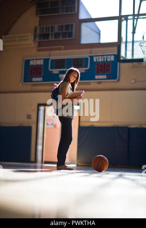 Teenage girl holding manuels debout sur un terrain de basket-ball Banque D'Images