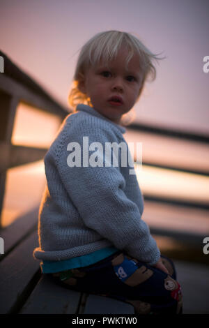 Portrait d'un jeune garçon vêtu d'un pull bleu à l'extérieur sur un balcon au coucher du soleil. Banque D'Images