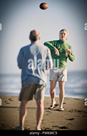 Man throwing a football avec un ami sur une plage de sable. Banque D'Images