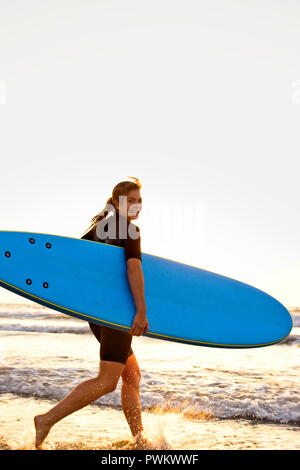 Jeune femme à l'approche du surf au coucher du soleil avec un surf. Banque D'Images