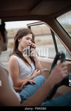 Jeune femme au téléphone pendant que son petit ami est assis dans la voiture Banque D'Images