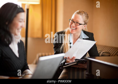 Deux jeunes femmes d'rire comme ils travaillent ensemble dans une chambre d'hôtel pour un voyage d'affaires. Banque D'Images