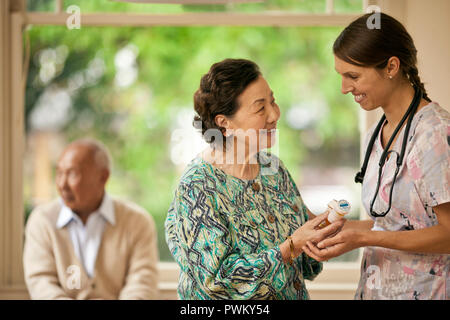 Smiling nurse donner a senior woman bouteilles de pilules. Banque D'Images