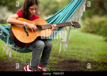 Jeune fille qui joue de la guitare sur un hamac dans le pays. Banque D'Images