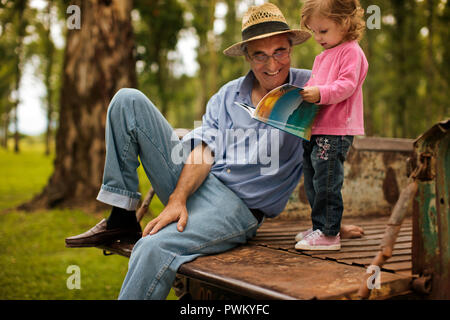 Petite fille à la recherche de livre photo avec son grand-père à l'arrière de sa camionnette. Banque D'Images