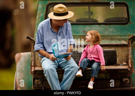 Petite fille à la recherche de livre photo avec son grand-père à l'arrière de sa camionnette. Banque D'Images