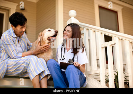 Heureux femme âgée assise sur l'escalier en face de la maison de repos avec son chien et l'infirmière. Banque D'Images