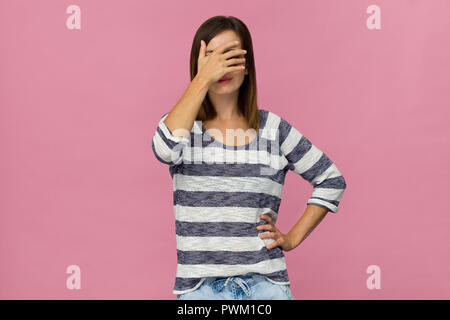 Belle jeune femme de race blanche cachant son visage dans sa main sur fond rose Banque D'Images