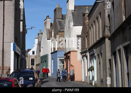 Les touristes parcourant la rue principale étroite de Stromness, Orkney, Scotland, un jour ensoleillé, passé grand-gris historique maisons en pierre et de boutiques colorées. Banque D'Images