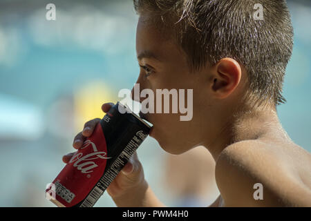 Un garçon est en train de boire un Coca-Cola peut. Photo de profil et en gros plans. Plage de Santa Giulia en Corse. Puszki Coca-ColChłopiec pije z ę. Banque D'Images