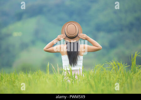 Woman traveler avec sac à dos, chapeau et regardant se trouve sur un pré, dans les montagnes. Banque D'Images