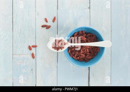 Baies de goji séchées sur une cuillère et dans un bol sur une surface rustique Banque D'Images