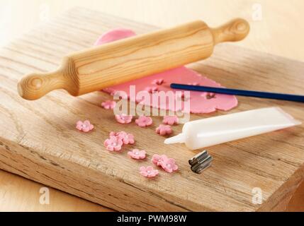 Pink icing déployé sur une planche avec un rouleau à pâtisserie, montrant une fleur en métal et coupe-tube de glaçage blanc Banque D'Images