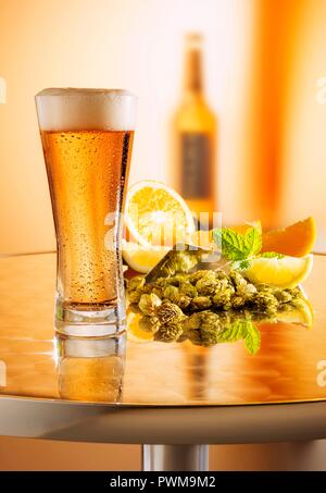 La bière fraîchement prélevé dans un verre sur une table en métal en face d'un arrangement de houblon, citrons et une bouteille de bière Banque D'Images