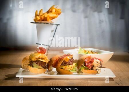 Trois mini-hamburgers sur un plat de service avec un cône de jetons dans l'arrière-plan Banque D'Images