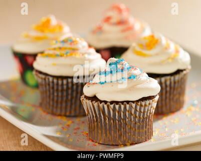 Petits gâteaux au chocolat avec glaçage à la vanille et de cristaux de sucre coloré sur un plateau ; Banque D'Images