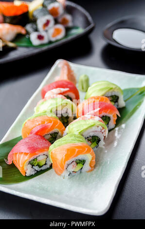 Plateau japonais de rainbow rolls maki, sur l'ALGUE et le rouleau de riz rempli de mayonnaise, concombre, avocat, crub stick surmonté de Salmo frais Banque D'Images