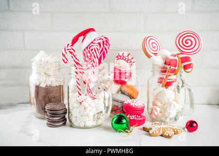 Ensemble de diverses friandises de Noël, épices, biscuits, macarons, guimauve au chocolat chaud ingrédients, en pot Mason lunettes, fond blanc co Banque D'Images