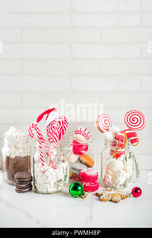 Ensemble de diverses friandises de Noël, épices, biscuits, macarons, guimauve au chocolat chaud ingrédients, en pot Mason lunettes, fond blanc co Banque D'Images