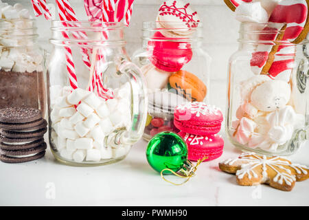 Ensemble de diverses friandises de Noël, épices, biscuits, macarons, guimauve au chocolat chaud ingrédients, en pot Mason lunettes, fond blanc co Banque D'Images