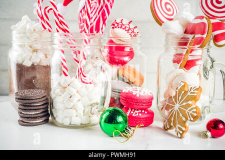 Ensemble de diverses friandises de Noël, épices, biscuits, macarons, guimauve au chocolat chaud ingrédients, en pot Mason lunettes, fond blanc co Banque D'Images