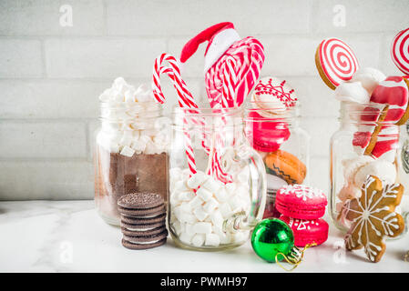 Ensemble de diverses friandises de Noël, épices, biscuits, macarons, guimauve au chocolat chaud ingrédients, en pot Mason lunettes, fond blanc co Banque D'Images