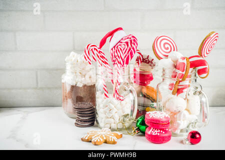 Ensemble de diverses friandises de Noël, épices, biscuits, macarons, guimauve au chocolat chaud ingrédients, en pot Mason lunettes, fond blanc co Banque D'Images