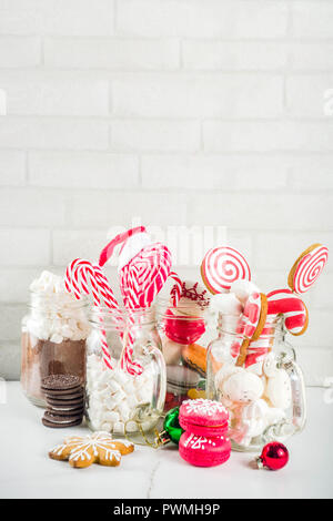 Ensemble de diverses friandises de Noël, épices, biscuits, macarons, guimauve au chocolat chaud ingrédients, en pot Mason lunettes, fond blanc co Banque D'Images