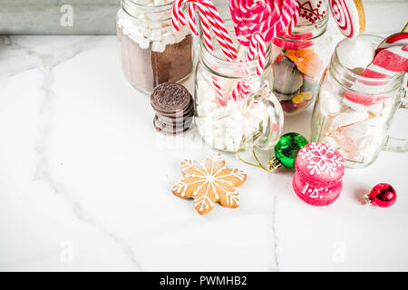 Ensemble de diverses friandises de Noël, épices, biscuits, macarons, guimauve au chocolat chaud ingrédients, en pot Mason lunettes, fond blanc co Banque D'Images