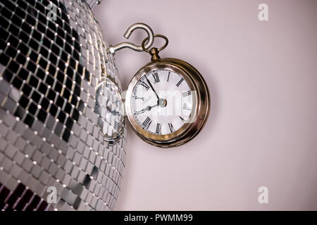 Arty shot d'une grande montre de poche en métal réveil à côté d'une boule disco argent Banque D'Images