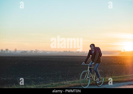 Circonscription de banlieue femelle un vélo à l'extérieur de la ville en zone rurale. Young woman riding bike au coucher du soleil Banque D'Images