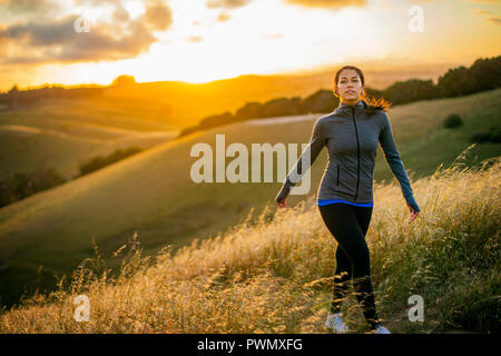 Jeune femme bénéficie d'une promenade à travers la campagne au coucher du soleil. Banque D'Images