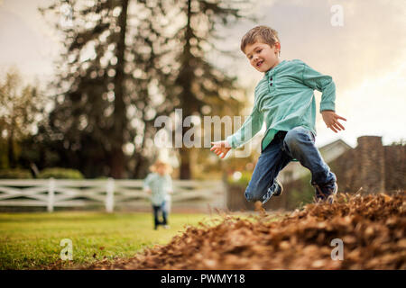 Jeune garçon sauter dans des tas de feuilles. Banque D'Images